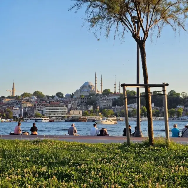 People sitting by the Golden Horn with the Süleymaniye Mosque behind